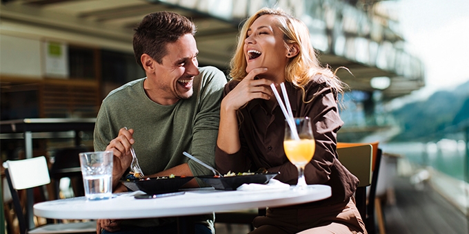 Una pareja riendo mientras come en un café al aire libre.