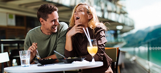Una pareja riendo mientras come en un café al aire libre.