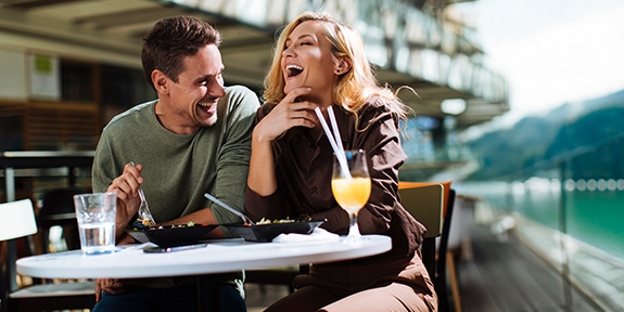 Una pareja riendo mientras come en un café al aire libre.