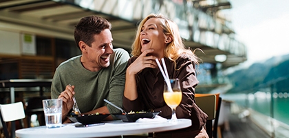 Una pareja riendo mientras come en un café al aire libre.
