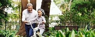 Little girl being taught how to ride a bicycle by her grandfather at the park.