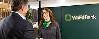 A smiling woman in a WaFd Bank uniform and a man in a black suit sitting together inside a modern WaFd Bank branch.