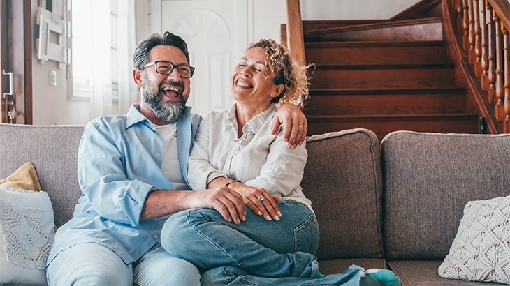 Couple laughing sitting on sofa in living room.