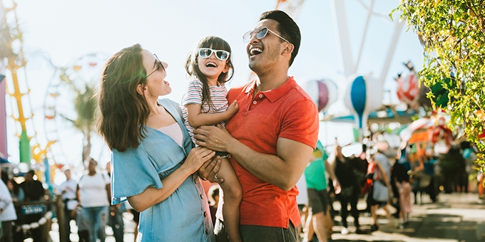 Parents holding their child while laughing at a carnival.
