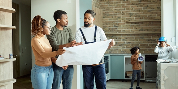 Couple looking at blueprints with contractor while kids play.