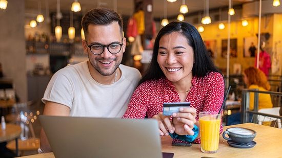 Happy couple in restaurant with laptop and credit card.