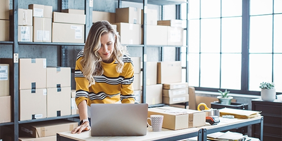 Female business owner on a laptop in a storage room.