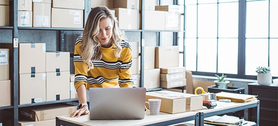 Female business owner on a laptop in a storage room.