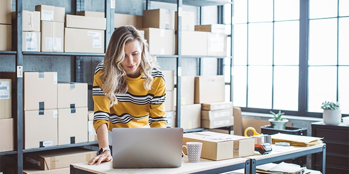 Female business owner on a laptop in a storage room.