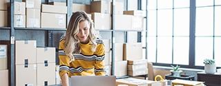 Female business owner on a laptop in a storage room.