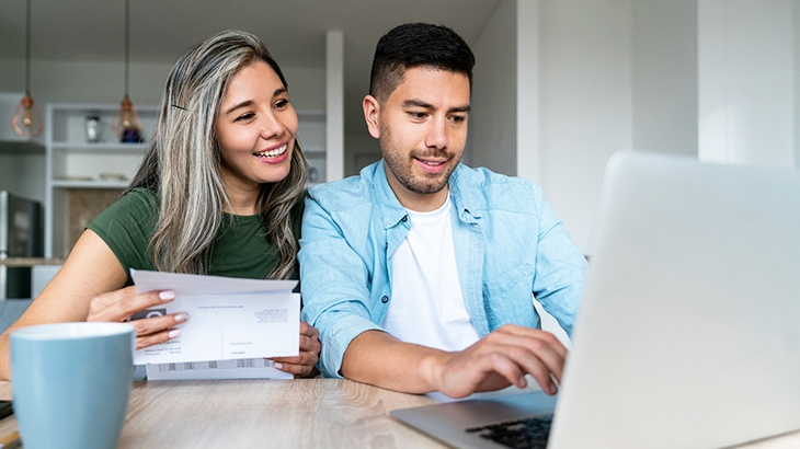 Happy couple at home paying bills online on their laptop.