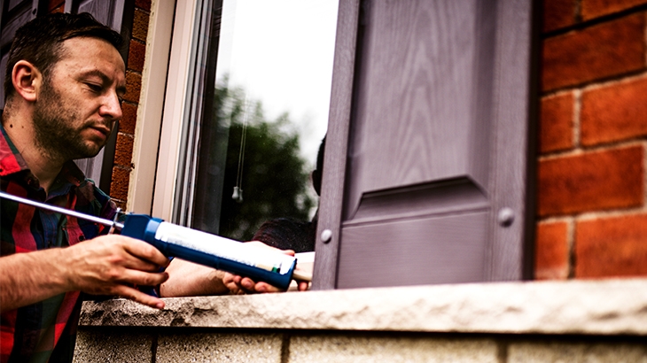 Man applying caulking around a window frame.