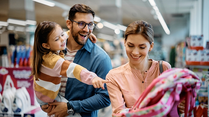 Girl pointing at backpack while buying school supplies with her parents.