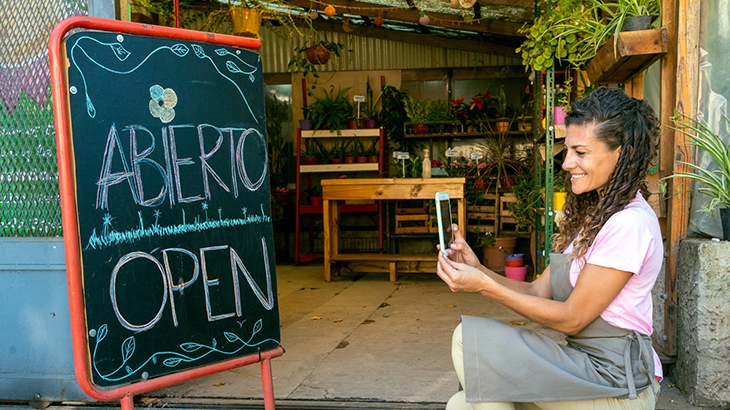 Shop owner taking photo of "Open" sign in front of small business store.