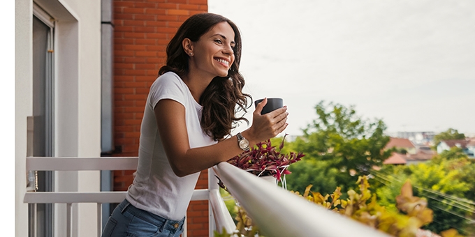 Young woman smiling while holding a coffee cup on a balcony.