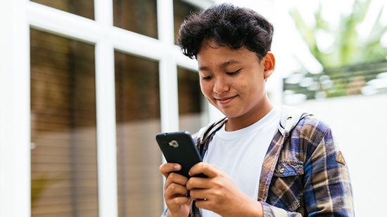 Smiling boy holding and looking at his mobile phone.