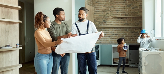 Couple looking at blueprints with contractor while kids play.