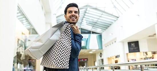 Man walking through a shopping mall with bags.