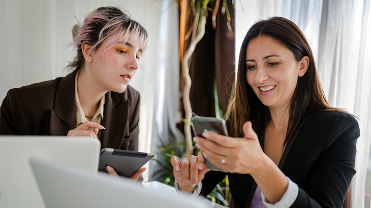 Two businesswomen working on a laptop and mobile phone.