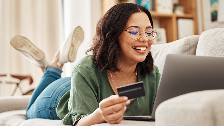 Woman laying on a couch while shopping with rewards card on her laptop. 