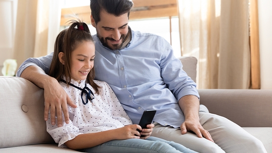 Padre e hija en un sofá mirando el celular.