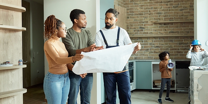 Couple looking at blueprints with contractor while kids play.