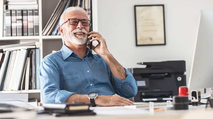 Business man smiling at his desk while talking on a phone. 