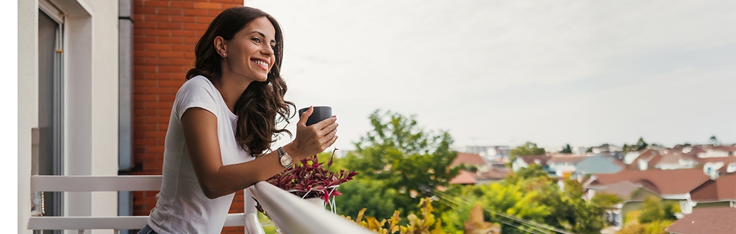 Young woman smiling while holding a coffee cup on a balcony.