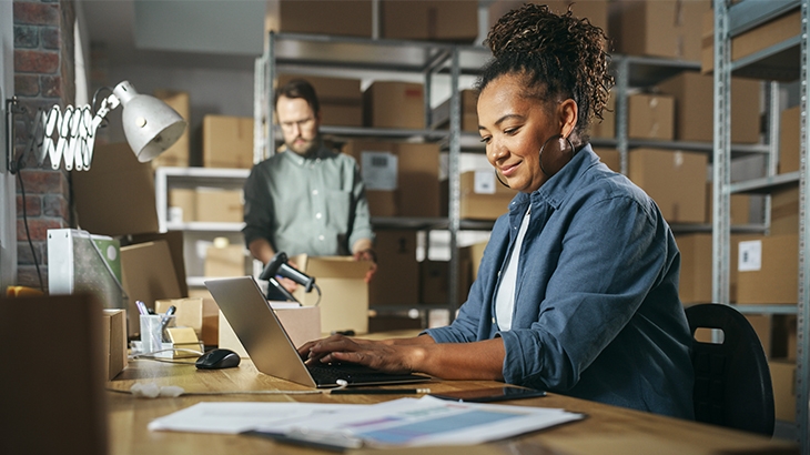 Businesswoman in a warehouse, working on a laptop.