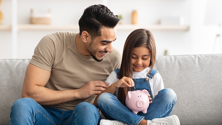 Father helping daughter count money for her piggy bank.