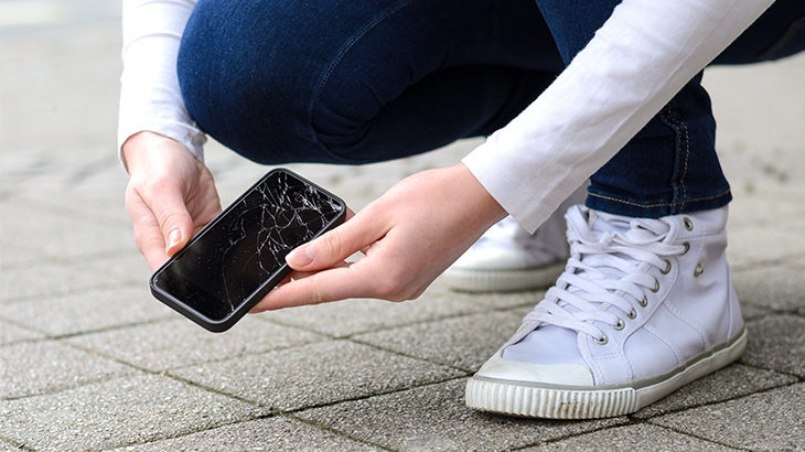 Kneeling person picking up a broken phone on the street.