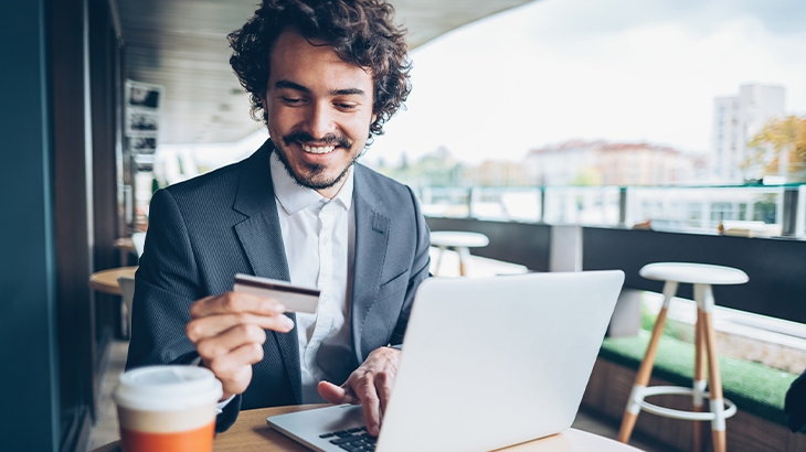 Businessman looking at credit card making purchase on laptop.