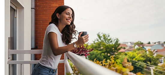 Young woman smiling while holding a coffee cup on a balcony.