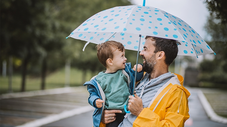 Father and son laughing under an umbrella on a rainy day.