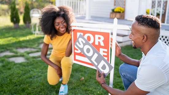 Couple next to a sold sign in front of their new house.