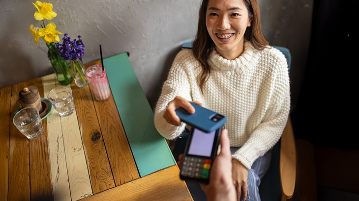 Customer smiling while making a mobile payment with her smartphone at a restaurant table.