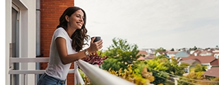 Young woman smiling while holding a coffee cup on a balcony.