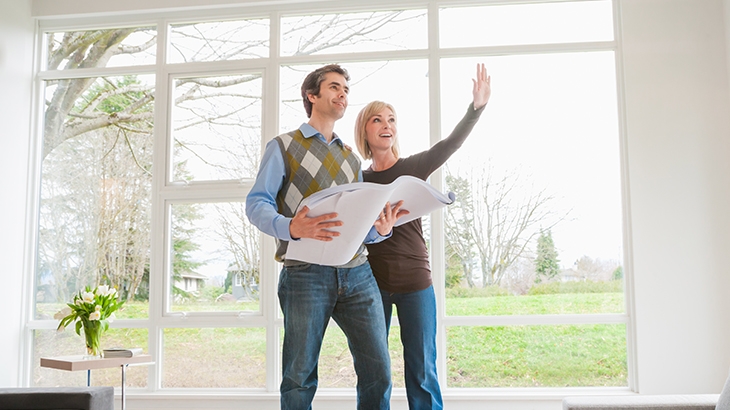 Couple holding building plans and discussing home remodel.