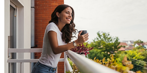 Young woman smiling while holding a coffee cup on a balcony.