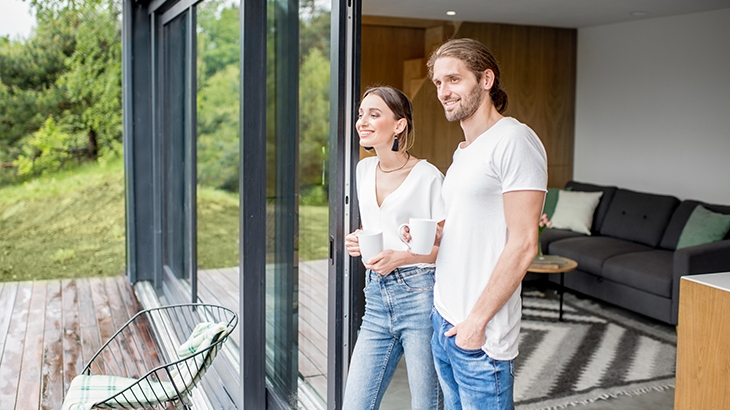 A happy couple standing in a glass doorway admiring their yard.