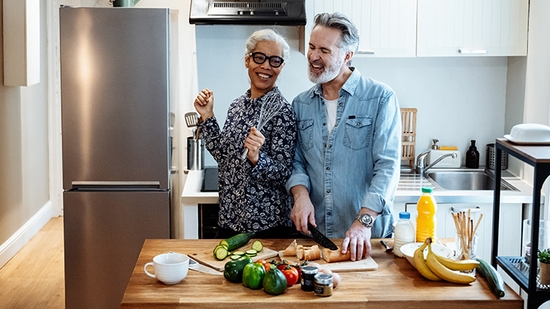 Pareja riendo mientras cocinan en su cocina.