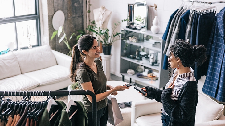 Woman holding her mobile phone making a payment at a clothing store.