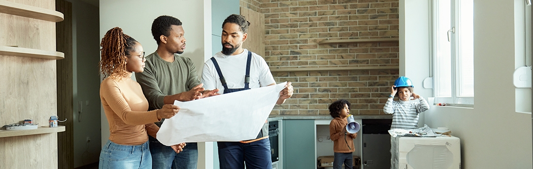 Couple looking at blueprints with contractor while kids play.