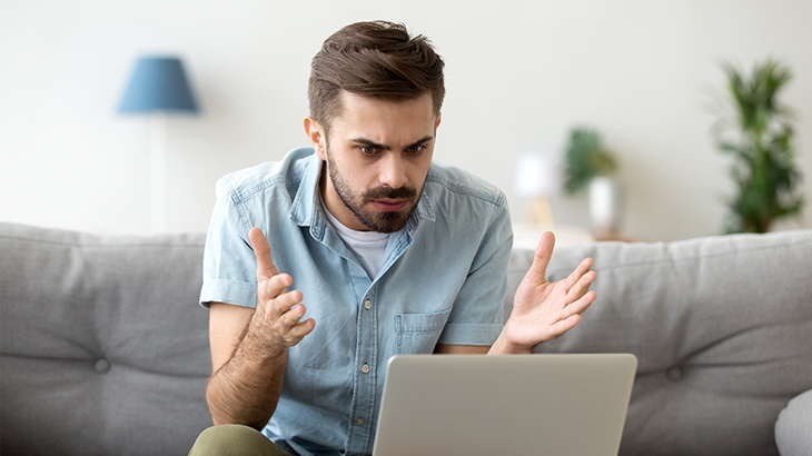 A frustrated man looking at a laptop.