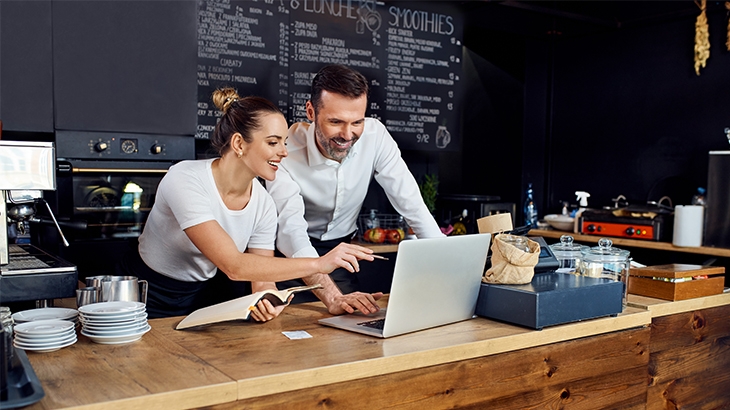 Coworkers reviewing analytics on a laptop in a cafe.