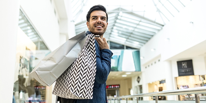 Man walking through a shopping mall with bags.