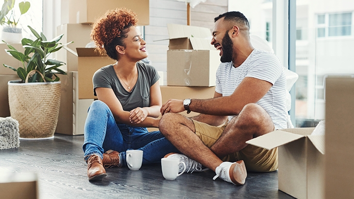 A couple sitting on the floor of their new house surrounded by boxes.