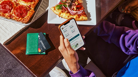 Overhead view of a teen holding a smartphone displaying the Greenlight app next to a Greenlight card, with pizza slices on a table.