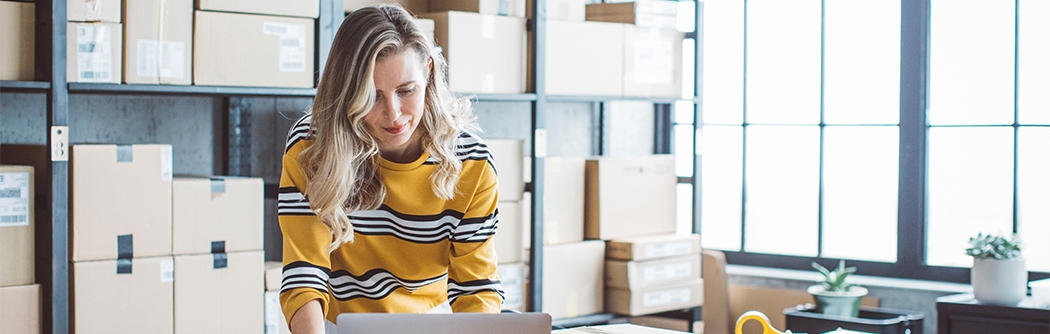 Female business owner on a laptop in a storage room.