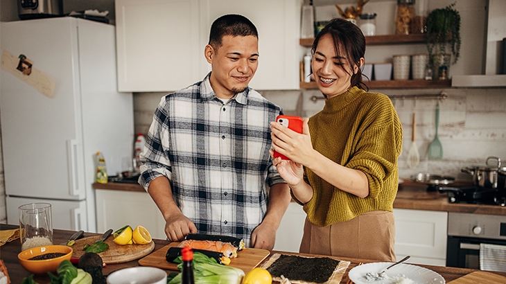 Couple looking at phone while cooking.